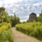 Gravel trail leading to stone windmill. Tall grasses on sides of trail.